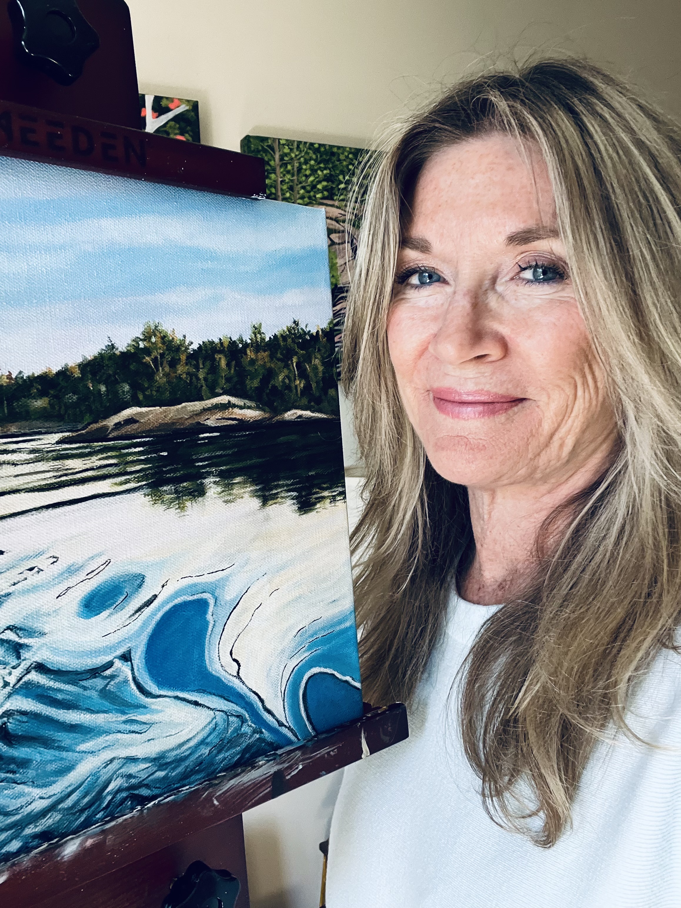 Joanne posing next to her landscape painting on an easel