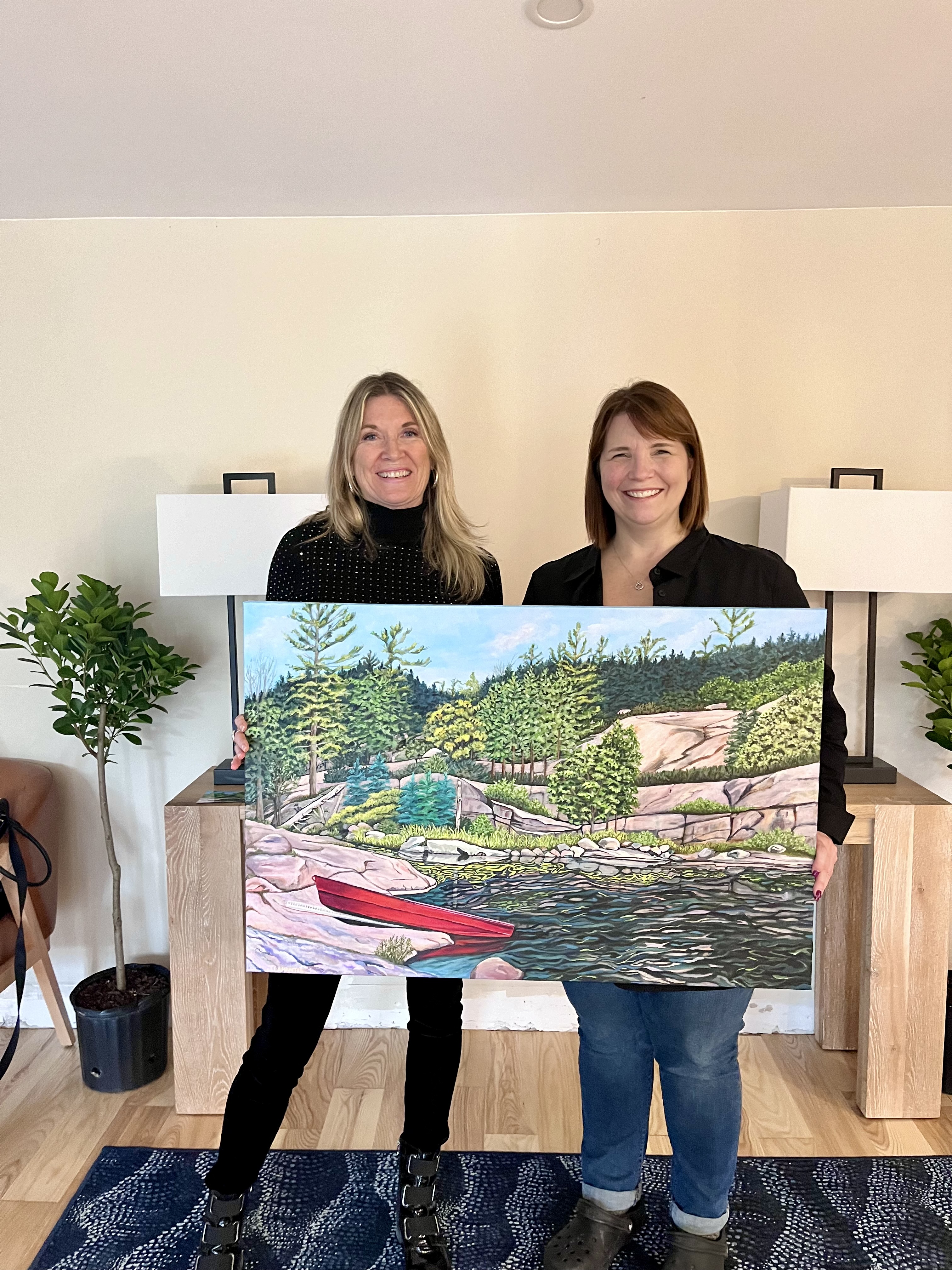 Two women holding a landscape commission painting